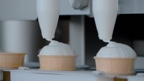 Super slow motion: automatic filling machine on ice-cream dairy factory - conveyor belt with icecream cones. Manufacturing, dairy industry, food processing and automated technology equipment concept