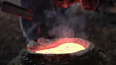 Worker Hand pouring Pieces of Metal into a Mold with Molten Liquid Metal in the Casting of Bronze Bells in a Foundry.