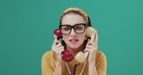 Woman holding two telephone receivers and listening to boring phone calls