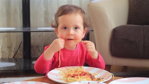 Little girl kid eating spaghetti pasta. Spaghetti pasta enjoyment with their hands. 