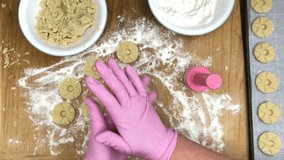 4K HD video Top view of gloved hands making pressed sugar cookies with an antique cookie press on a wood cutting board. Star imprint pattern