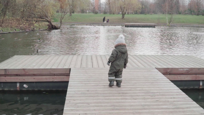 Boy in overalls on a floating pier feeding the ducks with bread