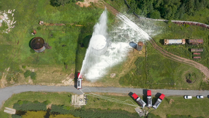 Firefighter or fireman on fire truck practicing at the training ground or range with fire extinguishing foam. Fire engine pours foam or shoots water