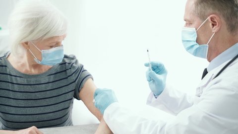 Get vaccinated. Male doctor wearing medical mask and gloves giving an injection to an elderly woman at the hospital