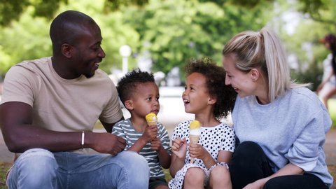 Multiracial family on walk in public park eating ice cream.