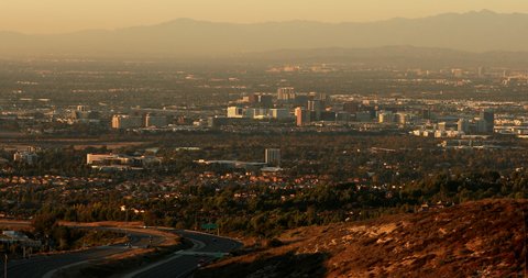 Twilight descends on the Orange County basin, casting the Irvine, Santa Ana, Costa Mesa, Orange, a and Anaheim skylines in warm light.