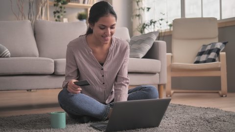 young smiling middle eastern woman sitting on the floor at home shopping on internet store using laptop,attractive adult mixed race female paying with credit card online banking e-commerce concept