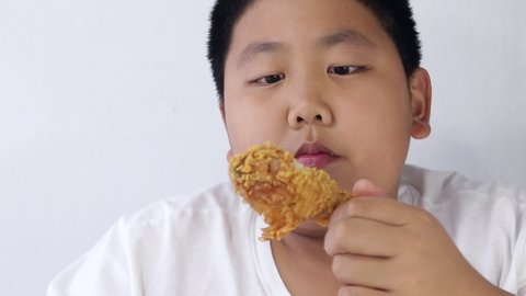 Asian fat boy eats fried chicken Wear a white shirt. Concepts of child health problems Pathogenic food
