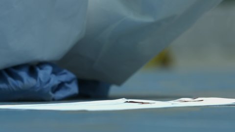 criminology investigator's hand with blue gloves, collecting blood samples at the crime scene with a cotton swab and inserting a pipette