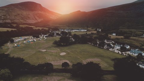 Sunset over mountain at village aerial. Nobody nature landscape at sun set. Cottages, houses at road. Whiskey distillery at valley. Cinematic Loch-Ranza, Arran island, Scotland, United Kingdom, Europe