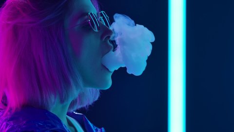 Portrait of a young stylish woman in sunglasses smoking a hookah and blowing out puffs of smoke. Close up. Slow motion.
