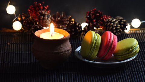 Three French macarons with candle light and holiday decorative ornaments in background, home alone during holiday season
