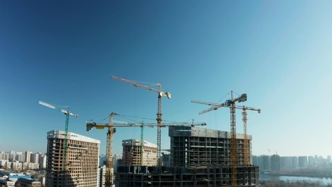 Fly over the construction site, work as construction personnel, builders work, construction houses. Aerial Flight Over a New Constructions Development Site with High Tower Cranes Building Real Estate.