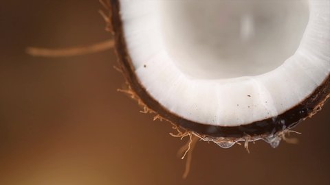 Coconut pouring water, dripping coconut milk, drops of coco nuts oil over brown background. Tropical Coco nut closeup. Healthy Food, skin care concept.