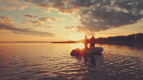 Friends fishing at sunset. Two amateur anglers fishing from the boat on a clam lake during sunset