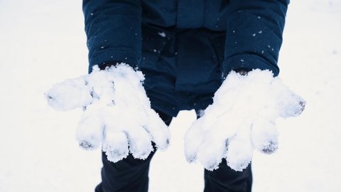 Close up man shakes off snow from his knitted gloves. Cold snowy winter in details.