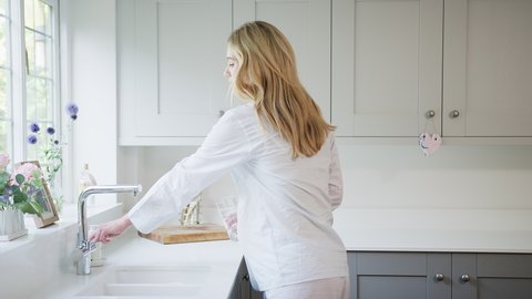 Loving couple with man hugging pregnant woman wearing pyjamas standing in kitchen holding bump and drinking glass of water - shot in slow motion