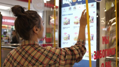 Woman types on fastfood restaurant interactive order board. Novosibirsk, Russia, 2020.