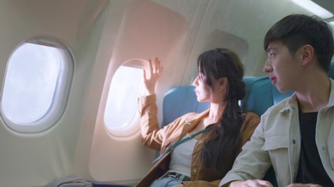 Asian young couple sit on window seat, looking and pointing outside. Man and woman feeling excited and happy for honeymoon sweet travel trip by airplane transportation.