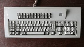 Typing on a big vintage Model F clicky terminal keyboard with 122 keys, battleship, making loud clicks due to buckling spring design. Fingers on both hands busy at work in the office. Video with sound