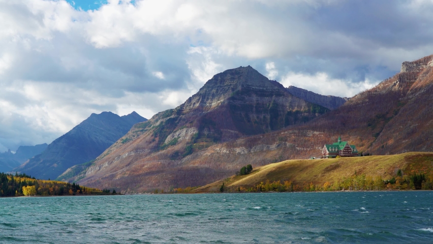 Middle Waterton Lake lakeshore in autumn foliage season sunny day morning. Blue sky, white clouds over mountains in the background. Landmarks in Waterton Lakes National Park, Alberta, Canada.