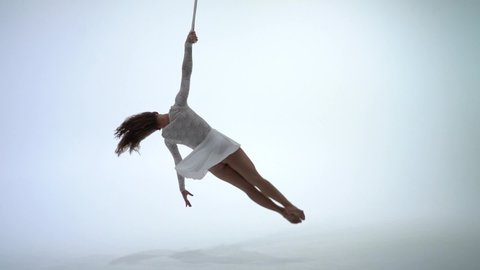 Female aerial straps artist doing performance on white background in slow motion. Concept of desire, elegance and grace 