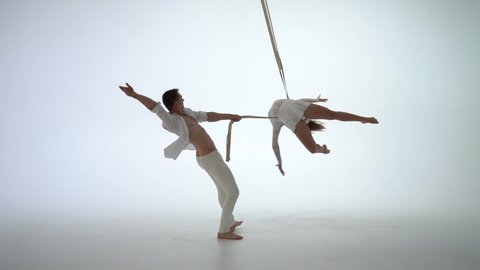 Aerial straps duo wearing white costume on white background doing performance in slow motion. Concept of desire, attraction and relationship