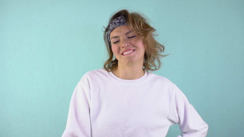 Slow motion: A cheerful, curly-haired woman throws an orange into the air, laughs and smiles, then throws the frame outside the orange. Woman on blue background.