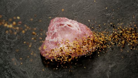 TOP VIEW: Spices fall on raw pork steak. Slow motion.