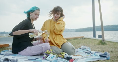 Two young woman in a loving gay relationship celebrating together outdoors on a rug overlooking the sea drinking wine and cuddling in a close embrace