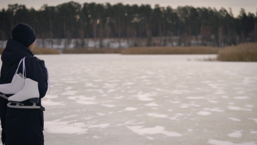 A young woman in a dark jacket, came to the frozen lake to go ice skating. In winter, nature can be fun.