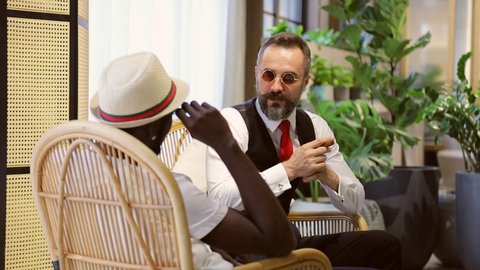 Caucasian businessman in formal wear and his African American friend in luxury tropical style hotel lobby