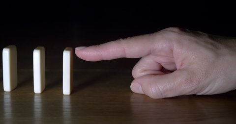 One hand drops white dominoes on wooden background. Concept of domino effect, chain reaction, risk management.