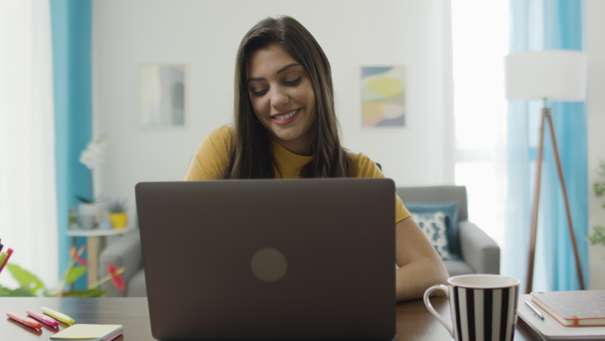 Lateral dolly of confident and cheerful caucasian brunette woman typing on a laptop. Young female professional writing an important email from her home in a modern living room with colorful elements Royalty-Free Stock Footage #1063587478