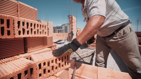 Professional worker rapidly gets red brick and place it on building wall. Fast moves