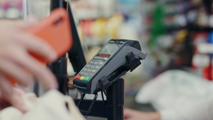 Close-up of young woman customer using phone for contactless wireless online credit card payment for purchases in supermarket store. Royalty-Free Stock Footage #1063591498