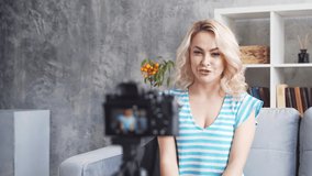 Young and attractive woman is recording video blog with a camera. Girl is sitting at home and vlogging.