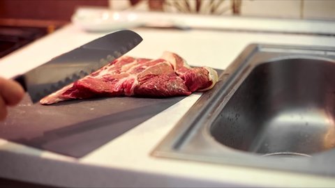 Human hands use a knife to cut meat. a man cuts up fresh meat for dinner in the kitchen