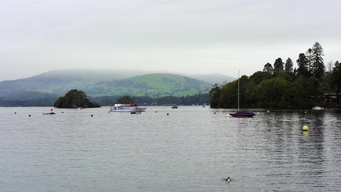 View of mist covered distant hills and mountains across the gentle waters of Lake Windermere in the English Lake District, Cumbria, England, UK.