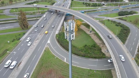 Traffic in slow motion on multilevel interstate overpass, all connected through 5G base station. Aerial.