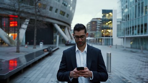 Close up businessman typing on cellular device walking home after work 