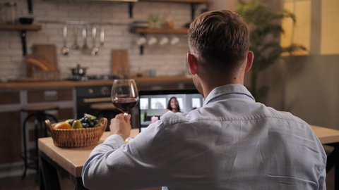 Attractive couple in love video chatting via webcam on laptop and clinking glasses with wine during romantic dating in quarantine. Happy caucasian male and mixed race female enjoying date at distance