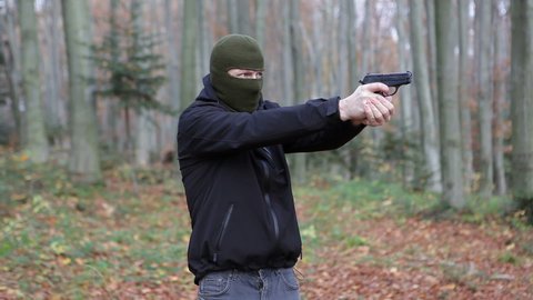 A man in a balaclava mask shoots a pistol in the forest.Video contains sound. One shot from a 9mm pistol.
