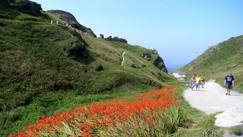 CORNWALL, ENGLAND, UNITED KINGDOM - CIRCA AUGUST, 2020: People walking from seaside up the gravel path, famous Tintagel castle visitors queuing on the hill, slow motion.