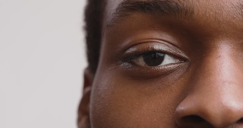 Close up half face portrait of african american guy looking seriously at camera, blinking eye, white studio background