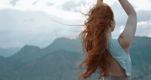 Carefree girl with red hair raising her hands up to the wind, embracing freedom and tranquility, enjoying scenic view of mountains 4k footage