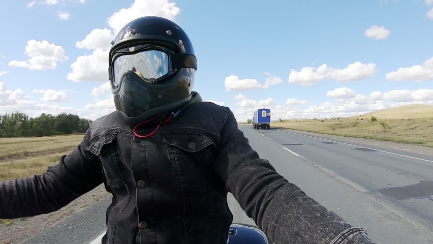 Man in helmet rides motorcycle on highway. Man with helmet and windproof glasses and clouds reflected in them is driving along highway against blue sky