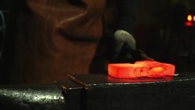 Close-up, a man strikes a red-hot metal with a hammer and forms a piece. Blacksmith at work. Craft. We make an ax. High quality 4k video