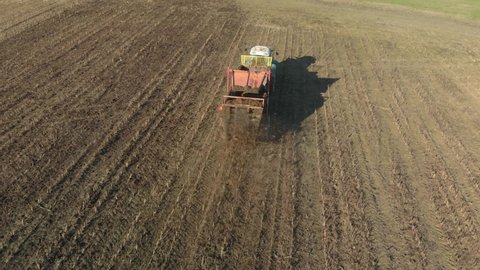 Tractor spreads organic fertilizers on brown fertile soil to increase productivity. Farmer with a farm machine on farmland in the fall or spring. Aerial view. Shooting from behind