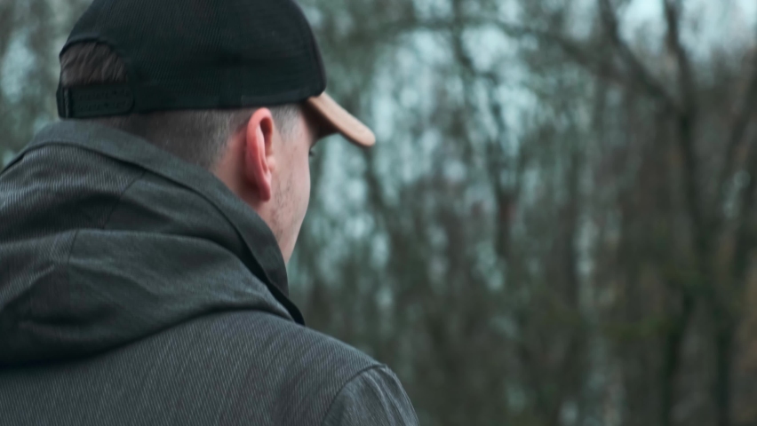 A young man walks along an empty city street wearing a baseball cap outside. Rear view of a man walking away through a city park. | Shutterstock HD Video #1063619062